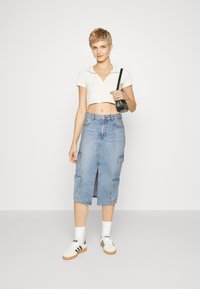Fustă midi din denim de culoare albastru deschis, cu buzunare tip cargo, slit frontal și talie ajustată. Asortată cu un top alb scurt și adidași.