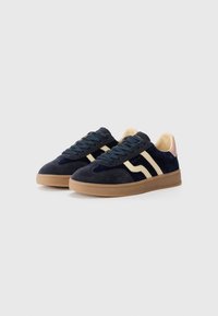 Marineblå ruskinn sneakers med kremfargede striper, rund tå, teksturert gummisåle, og kontrasterende rosa hælinnsatser. Strikkene og polstret krage er inkludert.