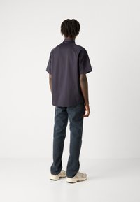 Camisa de mangas curtas, azul-marinho escuro, com bainha reta, combinada com jeans azuis e ténis de cor clara. Tecido suave com um corte descontraído.