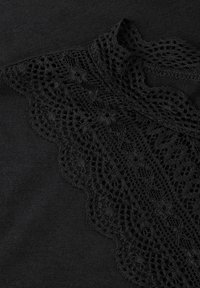 Schwarzer Stoff mit einer detaillierten Spitzenrüsche, die ein Karomuster und eine gewellte Kante am Ausschnitt aufweist.