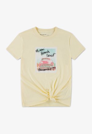 Tricou galben din bumbac, cu un nod în partea din față, având un design grafic cu o mașină vintage și textul „Apus de soare pe plaja Miami”.