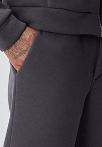 Sweat-shirt gris foncé avec fermeture éclair à l'avant, doté d'une poche latérale. Texture lisse et design décontracté avec une coupe ample.