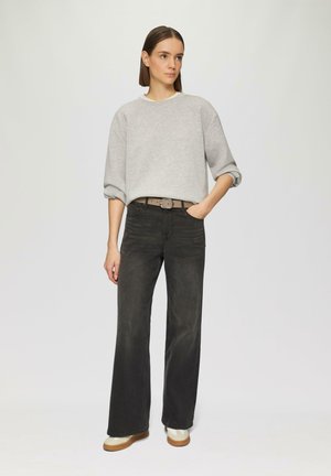 Grauer Pullover mit überschnittenen Schultern, kombiniert mit schwarzen, hoch taillierten, weiten Jeans und beigen Plattform-Sneakern. Elegantes und modernes Design.