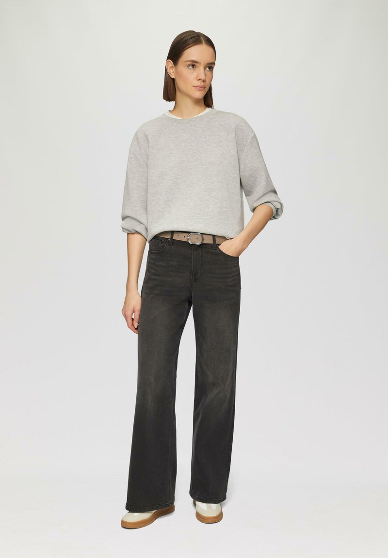 Grauer Pullover mit überschnittenen Schultern, kombiniert mit schwarzen, hoch taillierten, weiten Jeans und beigen Plattform-Sneakern. Elegantes und modernes Design.