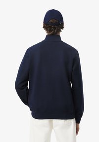 Marineblauwe sweatshirt met kraag en lange mouwen, met een soepele textuur en geribde zoom. Gecombineerd met een bijpassende pet.