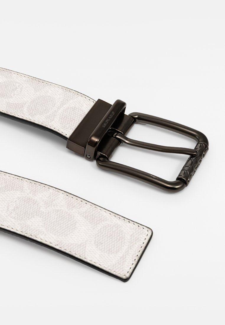 Ceinture avec une sangle en tissu à motif en blanc et beige, dotée d'une boucle en métal noir mat et d'accents texturés sur la dent.