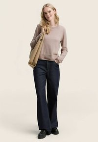 Világos rózsaszín kötött pulóver kerek nyakkivágással, sötétkék, bővülő szárú farmernadrággal párosítva. Bézs színű tote táska, fekete cipő.