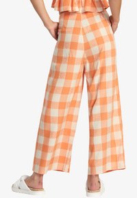 Široké nohavice v oranžovo-krémovej kockovanej vzore, vyrobené z ľahkej látky s kvetinovými detailmi, ktoré dopĺňajú ležérny letný vzhľad.
