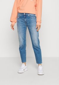 Jeans de mezclilla azul claro con corte recto, detalles desgastados y cinco bolsillos, combinados con un suéter melocotón y zapatillas blancas.