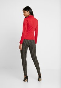 Casaco justo de manga longa vermelho com colarinho, combinado com leggings texturizadas em carvão com riscas verticais, usado com sapatos de salto alto pretos.
