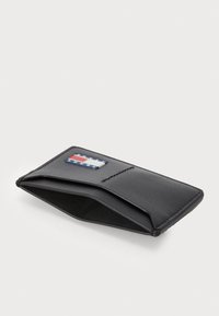 Μαύρο πορτοφόλι από υφή δέρμα, με ένα λογότυπο που διακοσμείται με κόκκινες, άσπρες και μπλε λεπτομέρειες. Λεπτός σχεδιασμός με κλείσιμο τύπου φλάντζας.