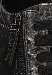 Acercamiento de un zapato de cuero negro texturizado con una cremallera metálica y cordones de tela negra.