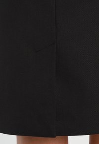 Sort nederdel i struktureret stof med et subtilt mønster og en sideslids for bevægelsesfrihed. Ren, skræddersyet design.