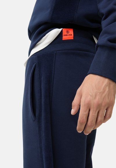 Marineblauwe joggingsbroek van zachte stof, met een oranje label, elastische tailleband, zijzakken en een textuurpaneel op het been.
