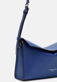 Blaue Lederhandtasche mit strukturiertem Design, schrägem Klappenverschluss und langem verstellbarem Trageriemen. Verfügt über silberne Hardware und bedruckten Markennamen.