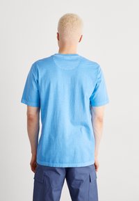 Světle modré bavlněné tričko s krátkým rukávem, kulatým výstřihem a uvolněným střihem. Tkanina má mírně texturovaný povrch.