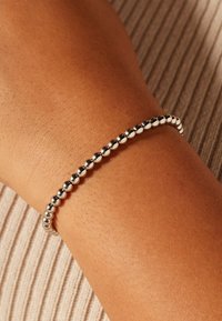 Zilveren armband met kralen om een pols, bestaande uit een reeks glanzende, ronde kralen met een gladde textuur tegen een neutrale achtergrond.