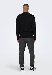 Schwarzer strukturierter Pullover, graue gestreifte Hose und Schwarz-Weiß-Sneaker. Der Pullover hat einen Rundhalsausschnitt sowie gerippte Bündchen und Saum.