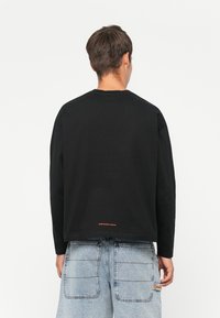Black long-sleeve t-shirt with a crew neckline, featuring a small orange "ENGINEERED WORKS" logo at the back hem. Textured cotton fabric.