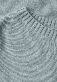 Lyseblå strikket trøje med ribkant ved halsen og en tekstureret, fintstrikket krop. Stoffet virker blødt med en glat finish.