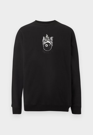 Črna majica crewneck s majhno belo grafiko goreče kroglice z osmico in besedo "MOTÖEN" pod grafiko.