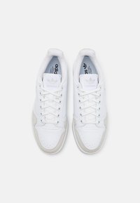 Hvide sneakers med en glat læderoverdel, grå ruskinds detaljer, perforeret tå og hvide snørebånd. Har Adidas-logoet på tungen.
