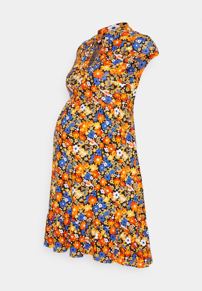 Kukkakuvioinen äitiysmekko, jossa on kauluksellinen pääntie, lyhyet hihat, vyötäröltä kiristetty malli ja levenevä helma eloisissa oranssin, sinisen ja keltaisen sävyissä.