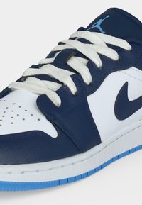 Χαμηλό sneaker με λευκή δερμάτινη βάση, σκουρό μπλε επικάλυψη, λευκά κορδόνια, μαύρο λογότυπο Nike και γαλάζια σόλα, εμφανίζοντας το επάνω μπροστινό τμήμα.