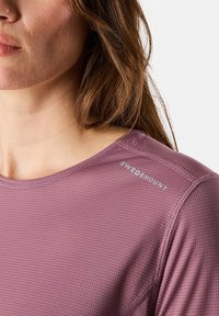 Paarse top met korte mouwen, voorzien van een gestructureerd patroon, een iets getailleerd ontwerp en het "SWEDEMOUNT"-logo op de schouder. Lichtgewicht stof.