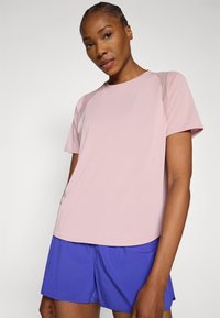 Αθλητική μπλούζα ανοιχτό ροζ με κοντά μανίκια και στρογγυλεμένη κάτω ραφή, με μικρό λογότυπο και αντίθετα ραφικά διακοσμητικά στοιχεία.