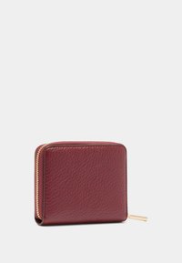 Portefeuille en cuir bordeaux avec une finition texturée, fermeture zippée et quincaillerie dorée. Forme carrée avec des bords arrondis.