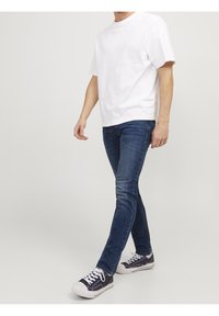 Vit bomulls t-shirt, avslappnad passform. Mörkblå slim jeans, denimtyg med lätt struktur. Marinblå sneakers med vit sula och snörning.