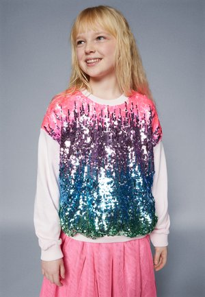 Sweatshirt pailleté avec un dégradé de sequins roses, violets, bleus et verts. Manches blanches et col côtelé. Associé à une jupe rose.