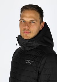 Giacca a vento nera con colletto alto e cappuccio. Presenta una chiusura a zip, cuciture orizzontali e un logo sul lato sinistro.