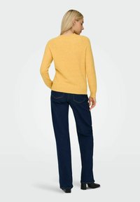 Yellow knit sweater with long sleeves, round neckline, and ribbed cuffs, paired with dark blue wide-leg jeans and black heels.