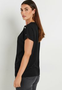 Short-sleeve black top with a round neckline, featuring a button detail on the shoulder and a smooth fabric texture.