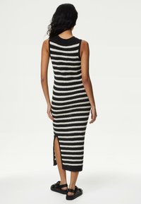 Pruhované pletené midi šaty v černé a krémové barvě, s bezrukávovým designem a bočním rozparkem. Texturovaná látka s přiléhavým střihem.