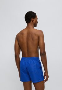 Μπλε μαγιό σορτς από ελαφρύ υλικό με ελαστική μέση, διαθέτει πίσω τσέπη και αντίθετες ραφές.