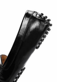 Chaussure en cuir verni noir au design élégant. Dotée d'une semelle texturée avec de petits accents arrondis et d'un dessus lisse.