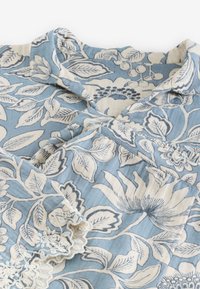 Blue fabric with cream floral and leaf pattern, featuring a folded collar and a sleeve with white lace trim.