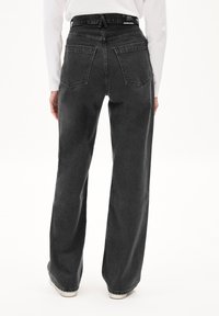 Zwarte jeans met wijde pijpen en een hoge taille, voorzien van achterzakken en een gestructureerde afwerking. De tailleband heeft een label en een naaddetail aan de achterkant.