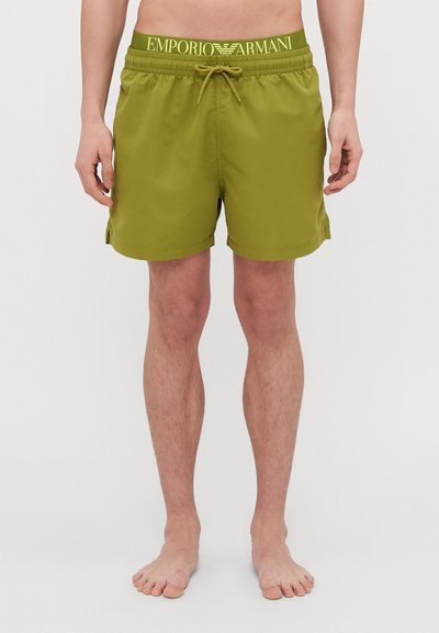 Shorts de bain verts avec une taille élastique arborant le logo "EMPORIO ARMANI". Fabriqués en tissu léger, arrivant au genou avec des fentes latérales.
