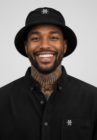 Black bucket hat with logo patch; textured fabric. Black button-up shirt with a collared neck and pocket, featuring matching logo.