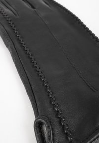 Guanto in pelle nera con una texture liscia, dettagli cuciti lungo il bordo e un design aderente senza chiusure o accenti.