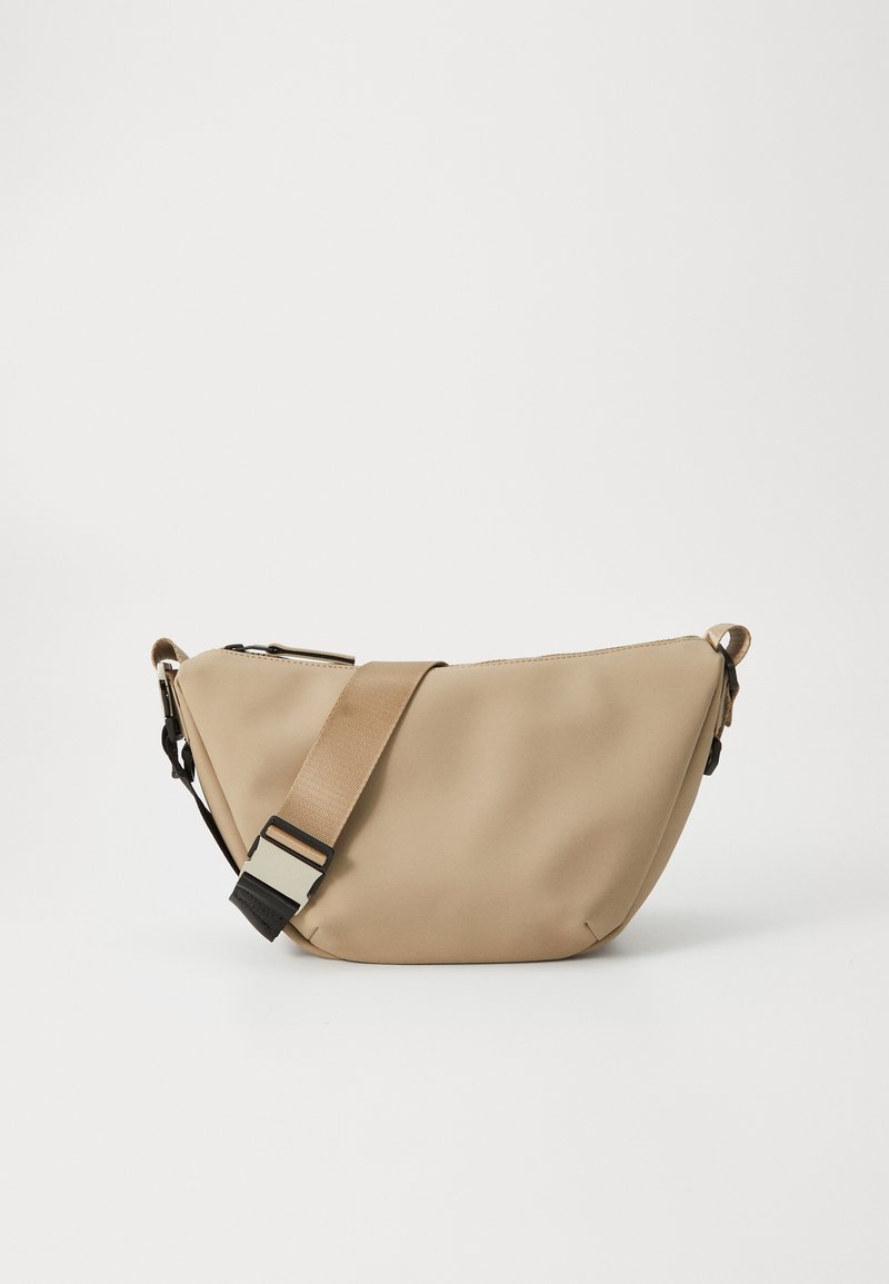 Bolsa crossbody bege com alça larga ajustável e fivela de plástico preta, apresentada sobre fundo branco liso.