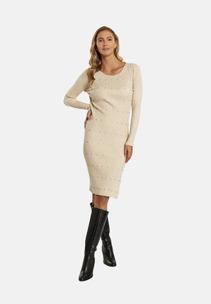 Knee-length béžové žebrované šaty s dlouhými rukávy, zdobené malými korálky; spárované s černými vysokými kozačkami.