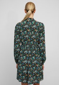 Blommig klänning med långa ärmar, med en svart bas och flerfärgade mönster i grönt, blått och orange. Midjan åtsmiten för passform.