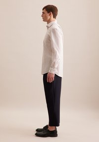 Camicia a quadri chiari in beige e bianco, abbinata a pantaloni neri affusolati. Il modello indossa scarpe in pelle nere. Tessuto morbido con una vestibilità strutturata.