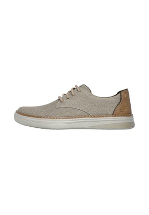 Zapato de lona beige con un upper texturizado, acento de cuero marrón en el talón, suela clara y cordones beige. Diseño clásico con cordones.