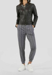 Giacca nera in pelle con zip abbinata a pantaloni grigi a fantasia, con polsini elastici e sneakers bianche per un look casual.